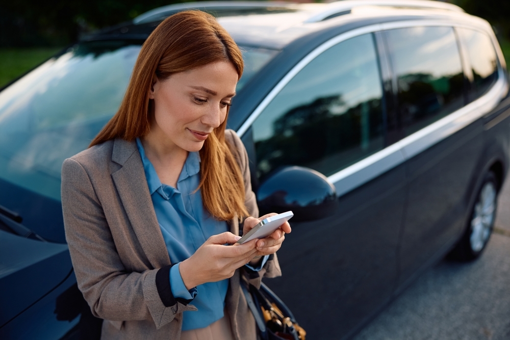 Mulher usando celular ao lado de veículo corporativo